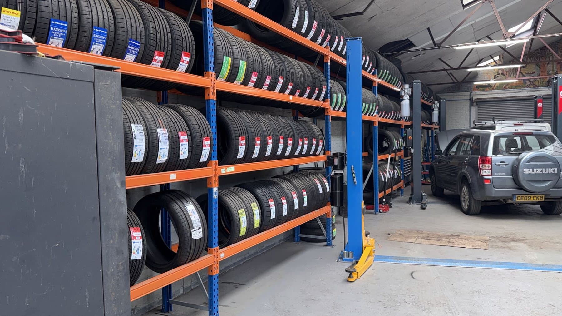 Workshop aisle with racked tyres and a two-post vehicle lift
